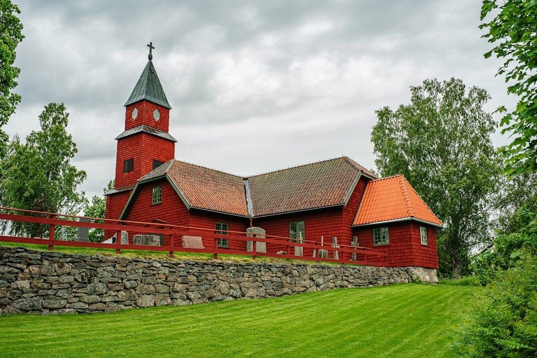 Röd träkyrka med klocktorn, omgiven av grönska under molnig himmel